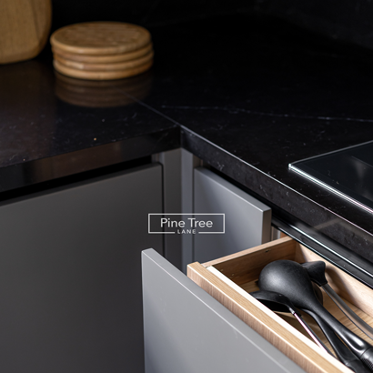 wooden drawer in a gray cabinet holds black kitchen utensils