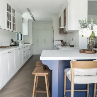 White kitchen cabinets with blue island and wooden dining stool