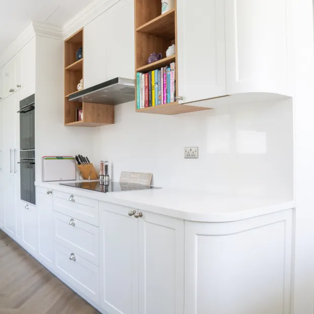 White kitchen cabinets with wooden floating shelves and integrated wall oven