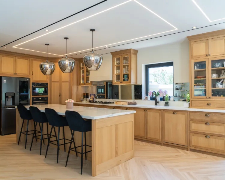 Modern wooden kitchen island with leather stools and warm custom cabinetry.