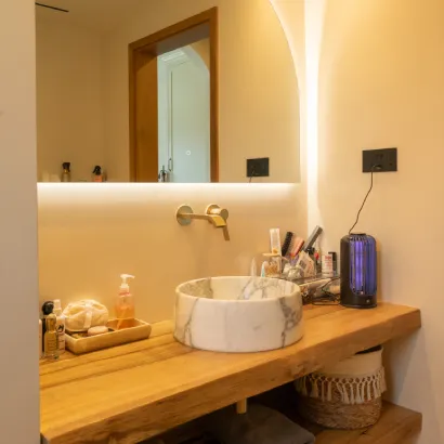 Modern wooden bathroom vanity with white marble vessel sink and backlit mirror